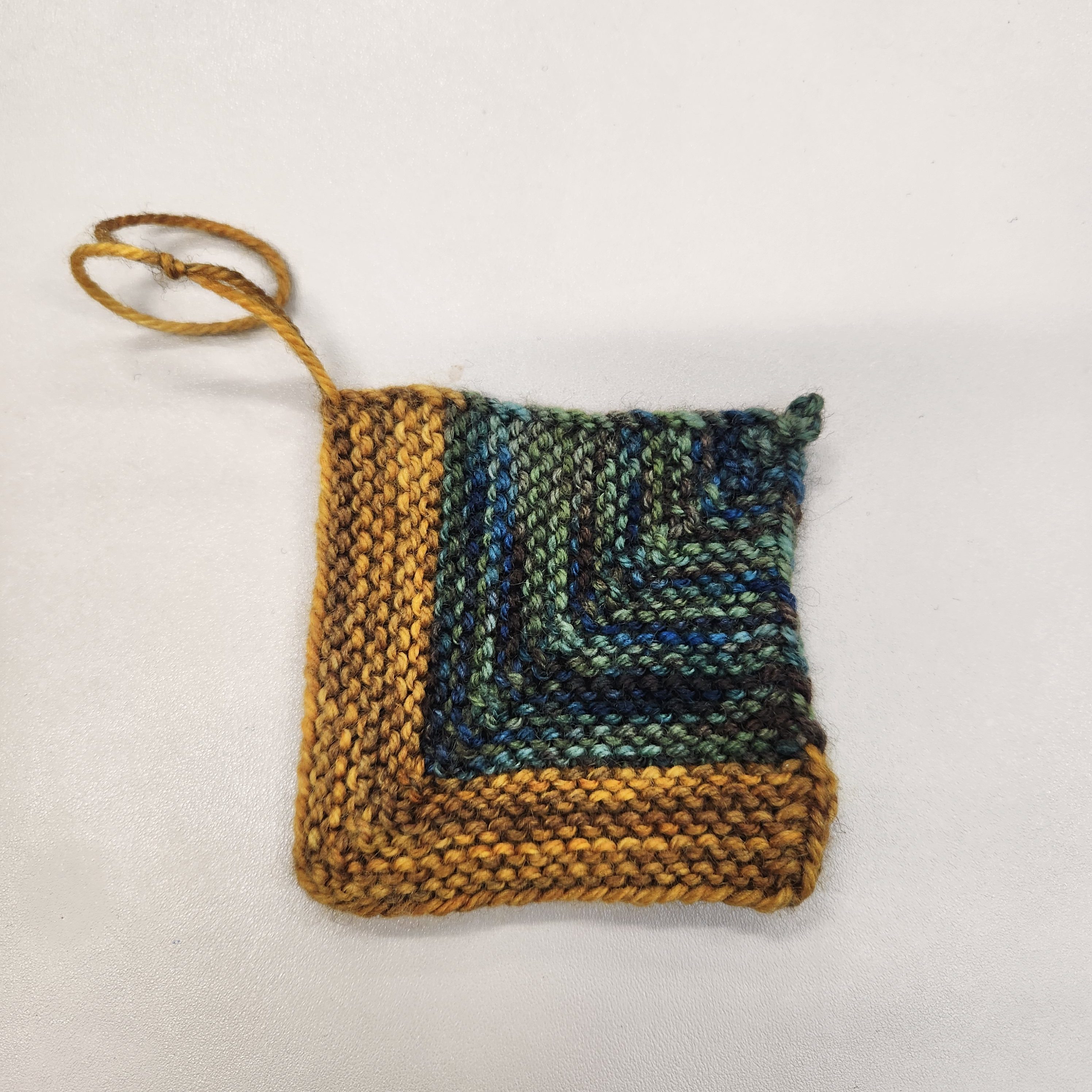 A knitted mitered square in gold and green